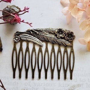 Puede incluir: Un peine para el cabello de plata y bronce con un diseño floral y de plumas. El peine tiene siete dientes y está decorado con tres pequeñas flores y dos plumas.