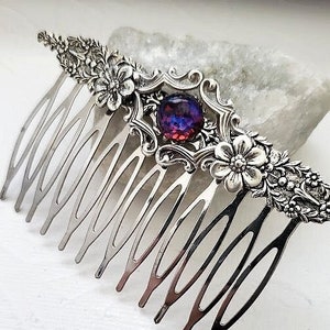 May include: Silver hair comb with a floral design and a purple and pink gemstone in the center.