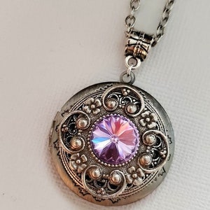 Puede incluir: Un collar con un medallón de plata con un delicado diseño de filigrana y una gran piedra preciosa púrpura iridiscente en el centro.