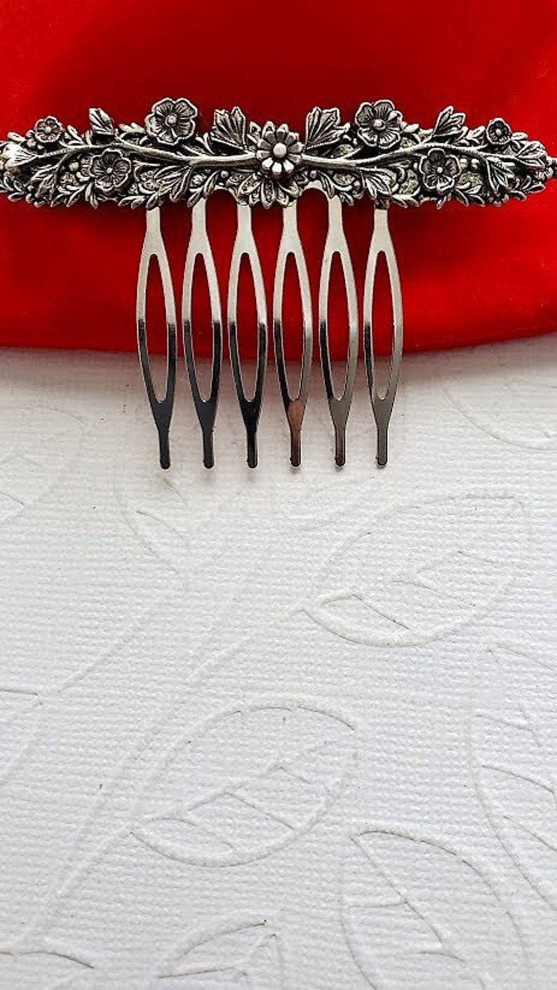 May include: Silver hair comb with a floral design. The comb has seven teeth and is decorated with leaves and flowers.