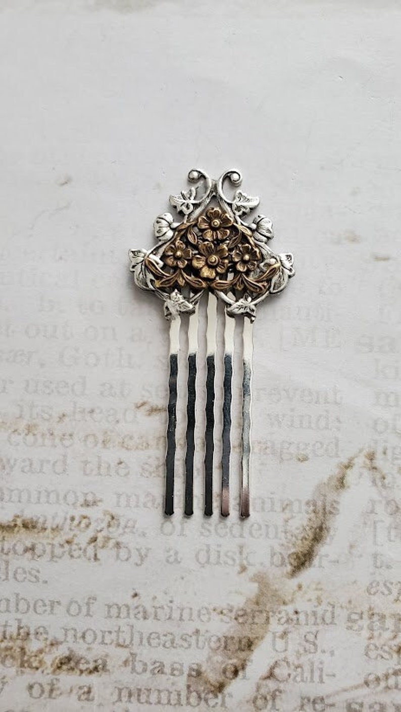 May include: A silver hair comb with a gold floral design. The comb has five tines and a decorative top.