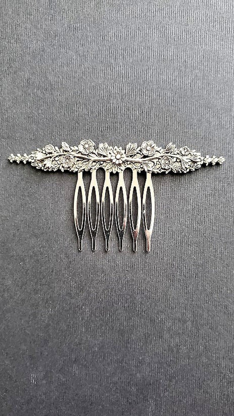 May include: Silver hair comb with a floral design. The comb has seven teeth and is decorated with intricate floral details.