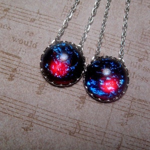 May include: Two silver necklaces with round, dark blue and red glass pendants. The pendants have a galaxy-like pattern with silver edging.