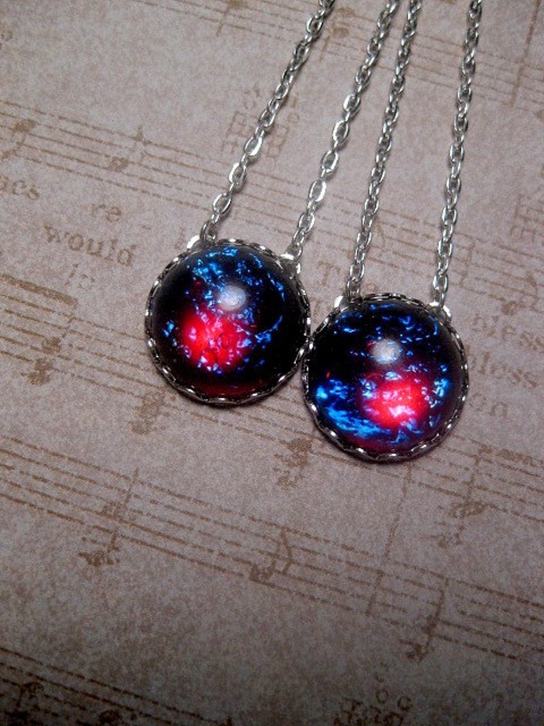 May include: Two silver necklaces with round, dark blue and red glass pendants. The pendants have a galaxy-like pattern with silver edging.