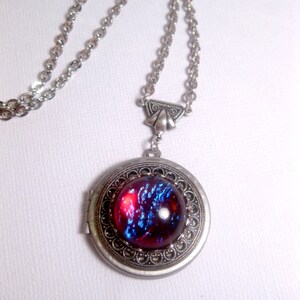 May include: A silver chain necklace with a silver locket pendant. The locket has a round, red and blue iridescent glass cabochon.