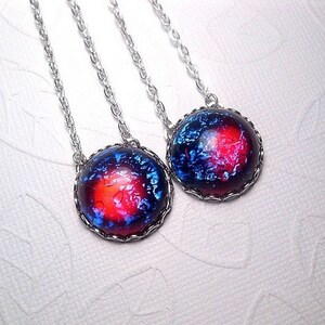 May include: Two silver necklaces with round, blue and red galaxy-themed pendants. The pendants have a black metal frame.