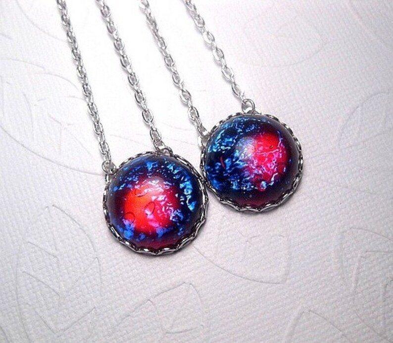 May include: Two silver necklaces with round, blue and red galaxy-themed pendants. The pendants have a black metal frame.