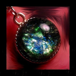 May include: A silver pendant with a round, iridescent glass orb. The orb has a dark green, blue, and black color scheme with a white, cloudy pattern.