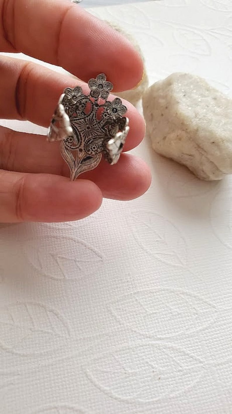 May include: A silver ring with a floral design. The ring is made of intricate filigree work and features several small flowers.