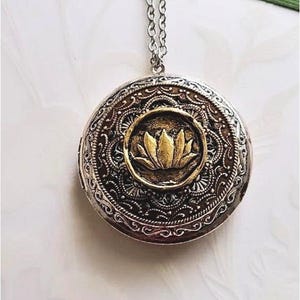 May include: Silver chain necklace with a round locket pendant. The locket has a silver and gold mandala design with a gold lotus flower in the center.