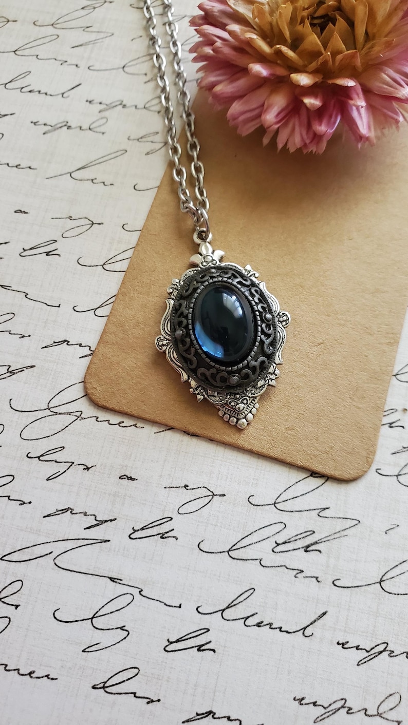 Peut inclure: Un collier en cha&icirc;ne argent avec un pendentif orn&eacute; d'une pierre ovale bleu fonc&eacute; sertie dans un cadre en filigrane argent.