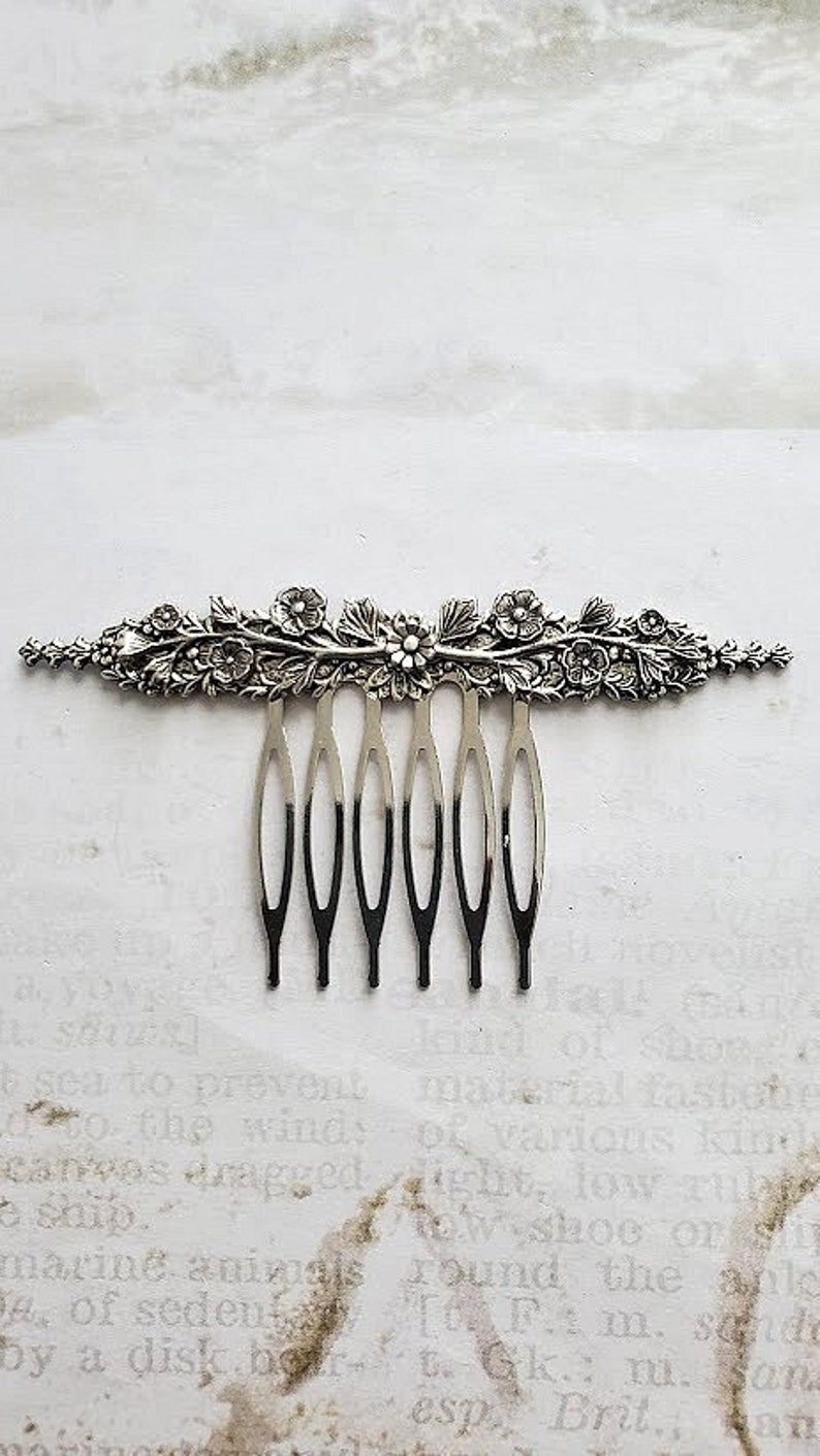 May include: Silver hair comb with a floral design. The comb has seven teeth and is decorated with a delicate floral pattern.