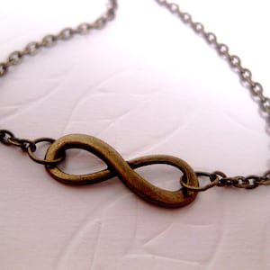 Puede incluir: Un collar de bronce con un símbolo de infinito y una cadena delicada.