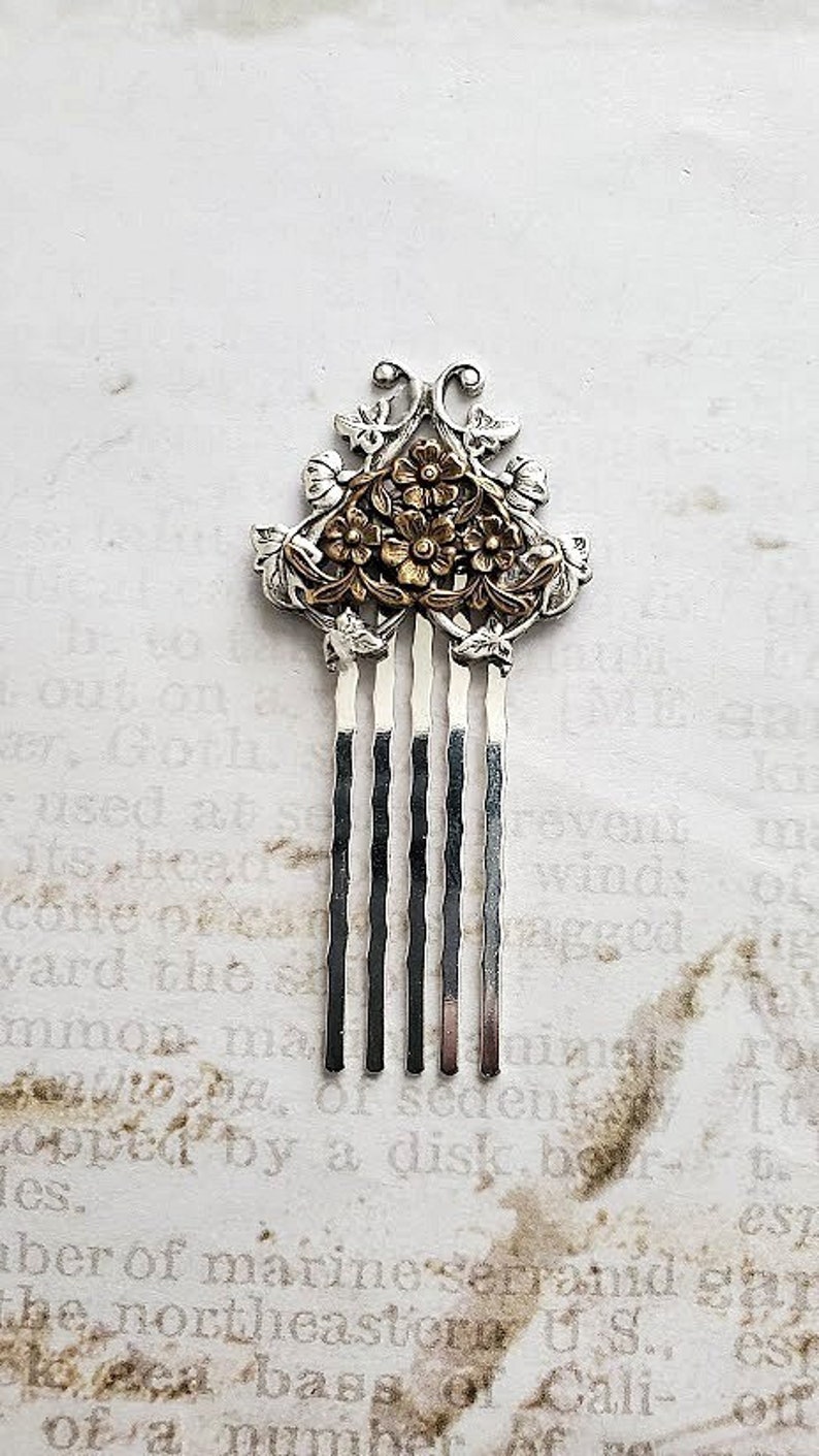May include: A silver hair comb with a floral design. The flowers are gold and have a raised design. The comb has five tines.