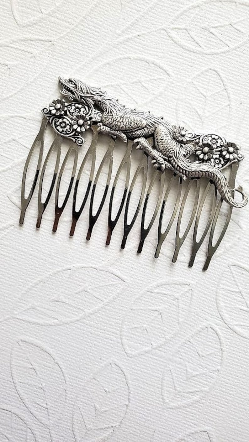 May include: Silver hair comb with a detailed dragon design. The dragon is curled around the comb and has floral accents.