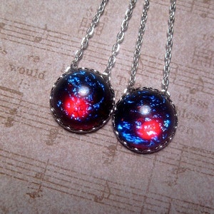 May include: Two silver necklaces with round, blue and red galaxy-themed pendants. The pendants have a silver rim.
