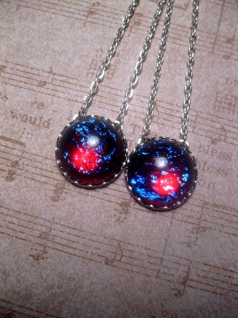 May include: Two silver necklaces with round, blue and red galaxy-themed pendants. The pendants have a silver rim.