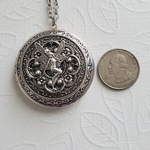 May include: Silver locket necklace with a detailed filigree design and a fairy charm. The locket is about the size of a quarter.