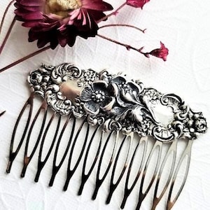 Puede incluir: Peine de pelo de plata con un diseño floral. El peine tiene un acabado plateado y presenta un patrón floral detallado con una flor central.