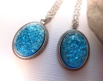 May include: Two silver necklaces with oval pendants featuring blue crackle glass. The glass has a sparkly, iridescent finish.