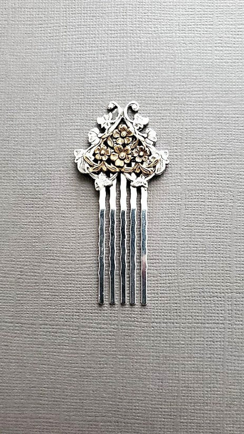 May include: A silver hair comb with a gold floral design. The comb has seven teeth.