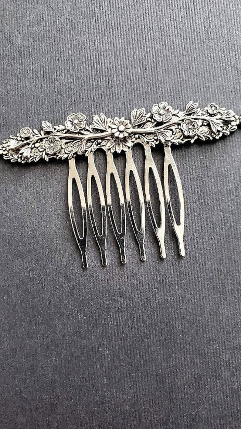 May include: Silver hair comb with a floral design. The comb has seven teeth and is decorated with intricate floral details.