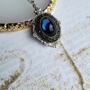 Peut inclure: Un collier en cha&icirc;ne argent avec un pendentif en pierre pr&eacute;cieuse bleu fonc&eacute; dans un cadre argent&eacute; orn&eacute;.