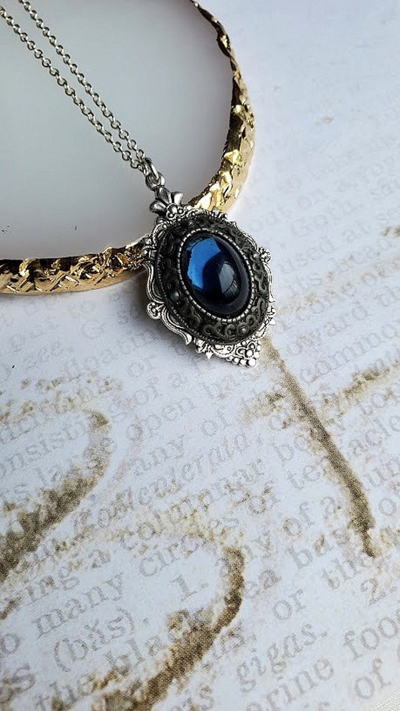 Peut inclure: Un collier en cha&icirc;ne argent avec un pendentif en pierre pr&eacute;cieuse bleu fonc&eacute; dans un cadre argent&eacute; orn&eacute;.