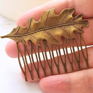 May include: A bronze-colored hair comb featuring a detailed oak leaf design. The leaf is intricately carved with veins and texture, and the comb has multiple tines for securing it in the hair. A decorative hair accessory.