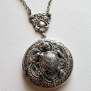 May include: A silver necklace with a locket featuring a detailed turtle design. The locket is ornate and has a delicate chain.