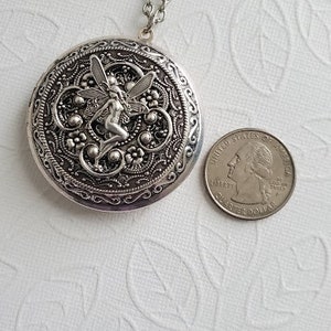 May include: Silver locket necklace with a detailed design featuring a fairy with wings. The locket is attached to a silver chain.