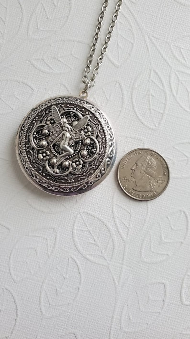 May include: Silver locket necklace with a detailed design featuring a fairy with wings. The locket is attached to a silver chain.