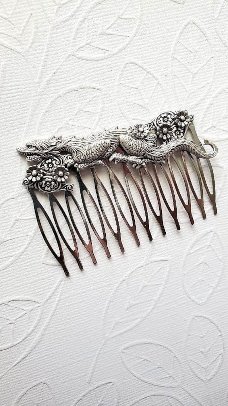 May include: Silver hair comb with a detailed dragon design. The dragon is curled around the comb and has floral accents.
