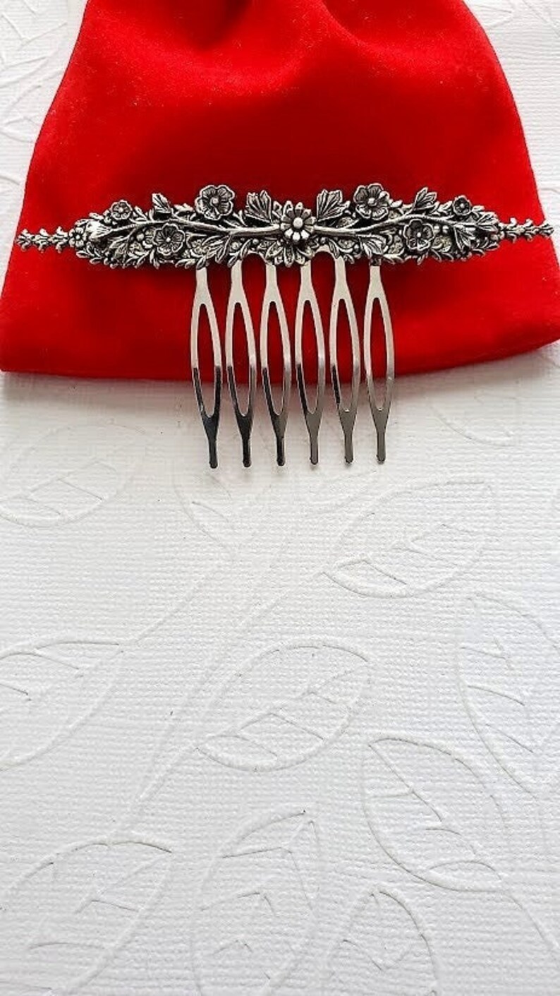 May include: Silver hair comb with a floral design. The comb has seven teeth and is decorated with leaves and flowers.