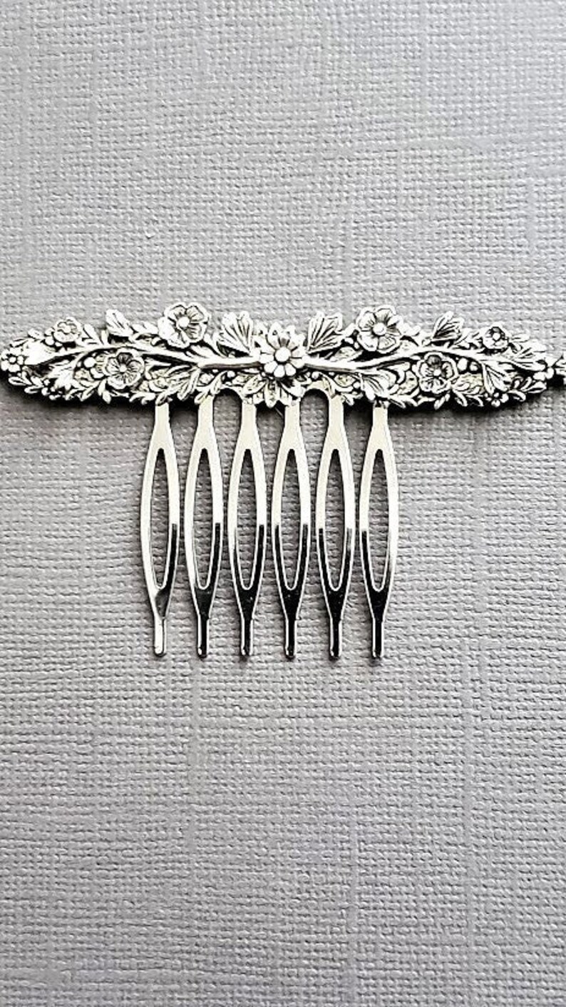 May include: Silver hair comb with a floral design. The comb has seven teeth.