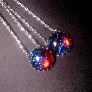 May include: Two silver chain necklaces with round blue and red glass pendants. The pendants have a swirling, galaxy-like pattern.