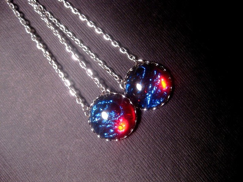 May include: Two silver chain necklaces with round blue and red glass pendants. The pendants have a swirling, galaxy-like pattern.
