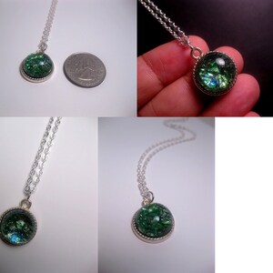 May include: A silver chain necklace with a green and blue iridescent glass pendant. The pendant is round and has a silver rim.