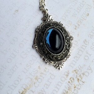 Peut inclure: Un collier en cha&icirc;ne argent avec un pendentif orn&eacute; d'une pierre ovale bleu fonc&eacute; sertie dans un cadre argent&eacute;.