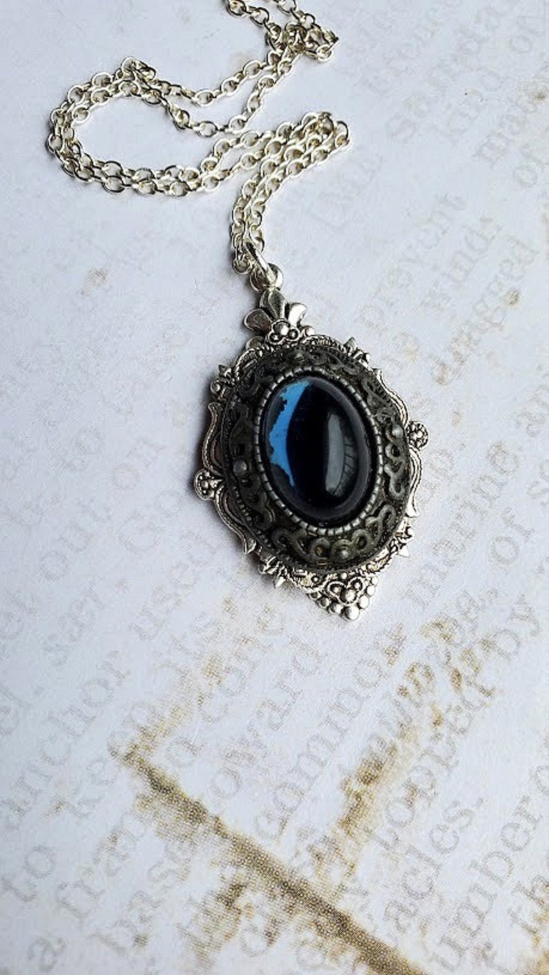 Peut inclure: Un collier en cha&icirc;ne argent avec un pendentif orn&eacute; d'une pierre ovale bleu fonc&eacute; sertie dans un cadre argent&eacute;.