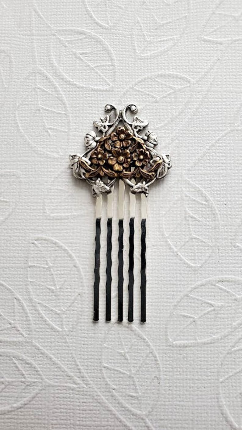 May include: A silver hair comb with a floral design. The flowers are gold and the comb has five tines.