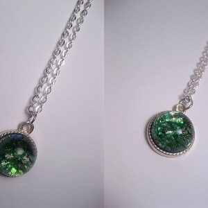 May include: A silver chain necklace with a round pendant featuring a green and silver glitter-filled resin cabochon.