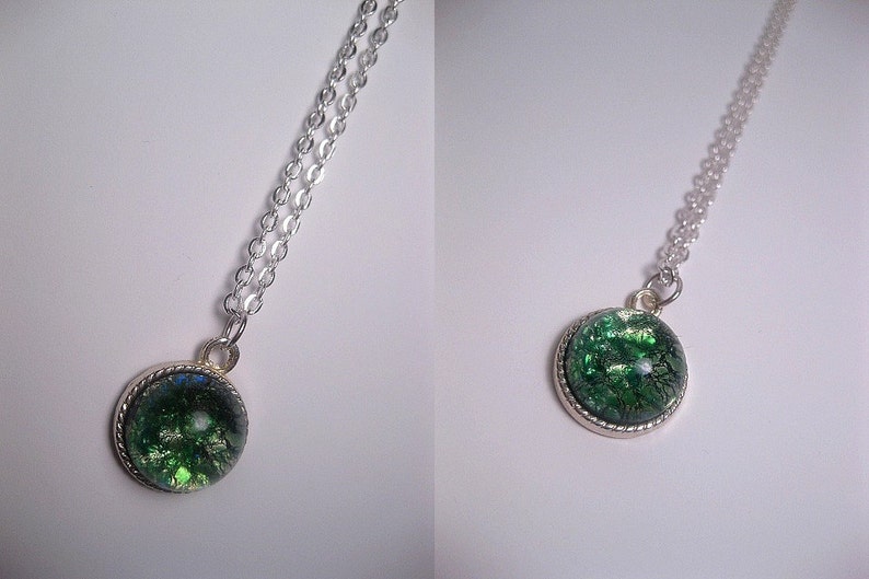 May include: A silver chain necklace with a round pendant featuring a green and silver glitter-filled resin cabochon.