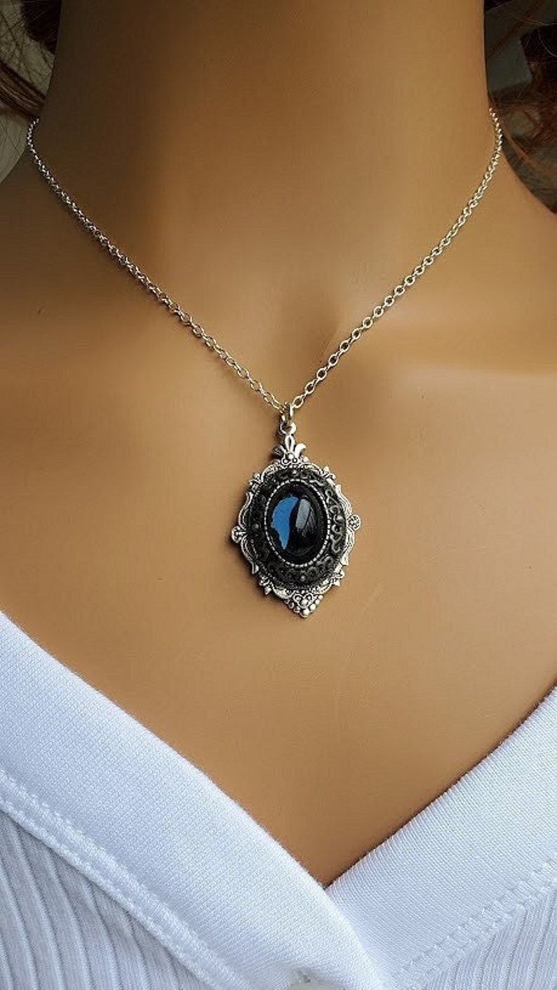 Peut inclure: Un collier en cha&icirc;ne argent avec un pendentif ovale noir orn&eacute; d'un motif de papillon bleu. Le pendentif est serti dans un cadre en filigrane argent.