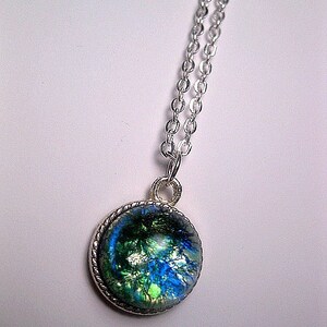 May include: A silver chain necklace with a round pendant featuring a blue, green, and gold iridescent glass design.