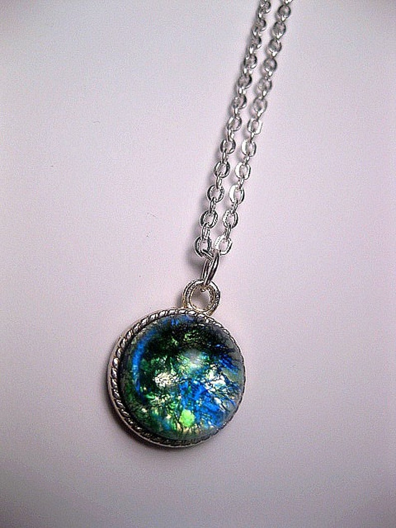 May include: A silver chain necklace with a round pendant featuring a blue, green, and gold iridescent glass design.