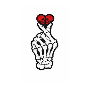 May include: A white and black patch featuring a skeleton hand forming a heart shape. Two red skulls are in the center of the heart. The patch has a black border and is set against a white background.