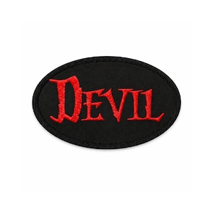 May include: Black oval patch with the word "DEVIL" embroidered in red, gothic-style lettering. The patch has a black border and is likely designed to be sewn or ironed onto clothing or accessories.