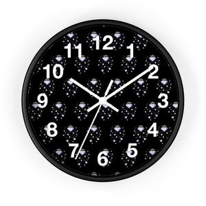May include: Black round wall clock with white numerals and hands. The clock face features a repeating pattern of diamond and crown designs. The clock has a black frame.