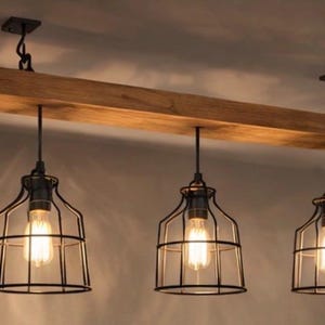 May include: A three-light pendant fitting with a rustic design. A light-brown wooden beam supports three black, cage-style light fittings. Each fitting has a visible Edison-style bulb. Designed for ceiling mounting.